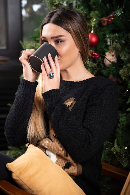 Young woman sitting on modern chair relaxing and drinking coffee or tea. High quality photo