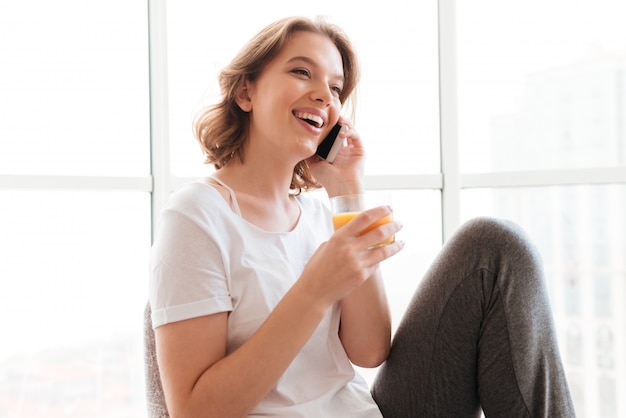 電話で話しているジュースを飲んで窓の近くに座っている若い女性