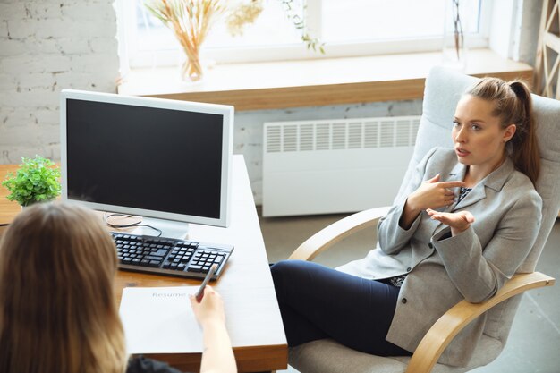 Young woman sitting in office during the job interview with female employee, boss or HR-manager, talking, thinking, looks confident
