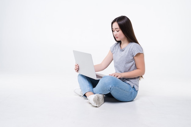 흰 벽에 고립 된 노트북과 함께 바닥에 앉아 젊은 여자