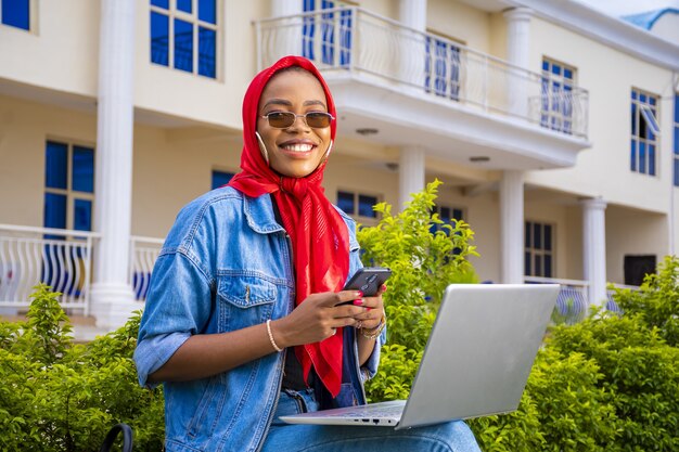 Young woman sitting outside with her laptop and phone