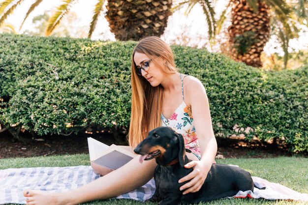 彼女の犬の読書で公園に座っている若い女性