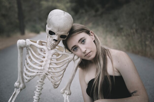 Young woman sitting on road with skeleton