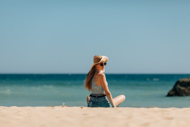 Young woman sitting on sand and looking to a sea. Rear view