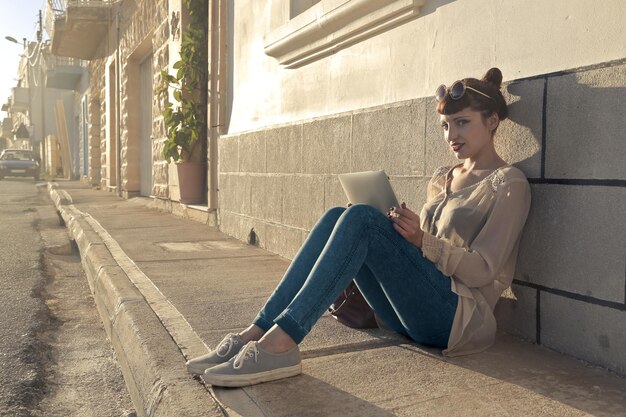 young woman sitting on the sidewalk uses a tablet