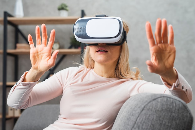 Молодая женщина, сидя на диване опыт с виртуальной реальностью
