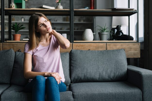 Young woman sitting on sofa having neck pain