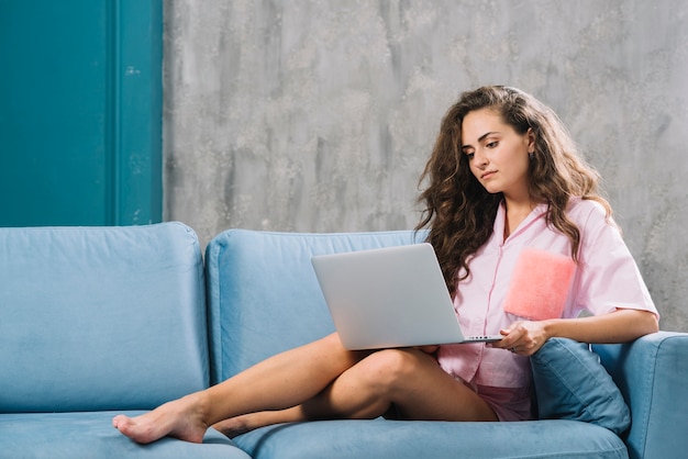Young woman sitting on sofa using laptop