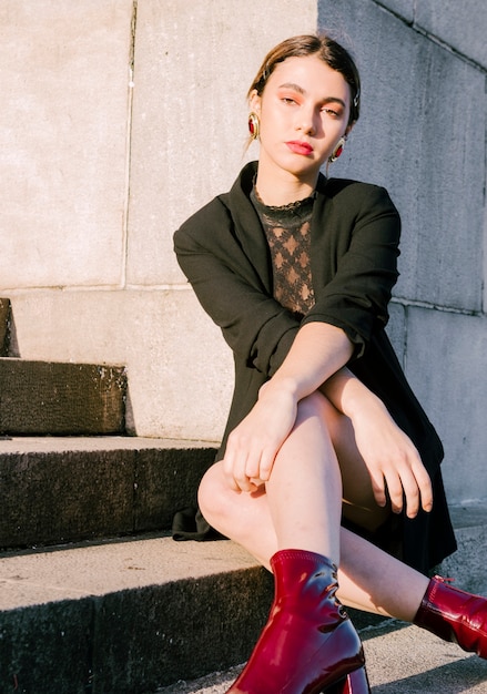 Free photo young woman sitting on staircase looking at camera with her crossed hands