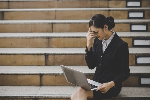 ラップトップコンピュータを使用して階段に座っている若い女性。屋外でラップトップで働く女性