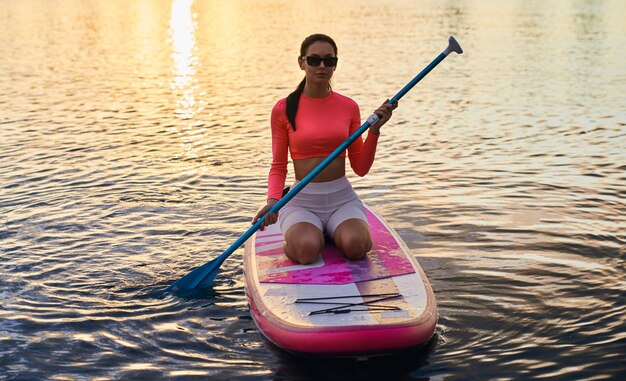 Young woman sitting on sup board on city lake