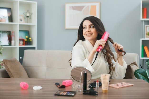 Young woman sitting at table with makeup tools in living room