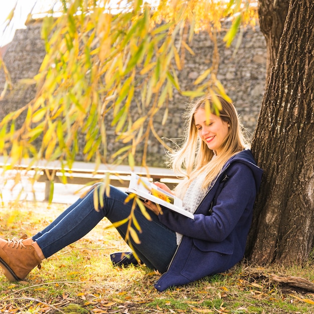 木の枝の下に座って読書する若い女性