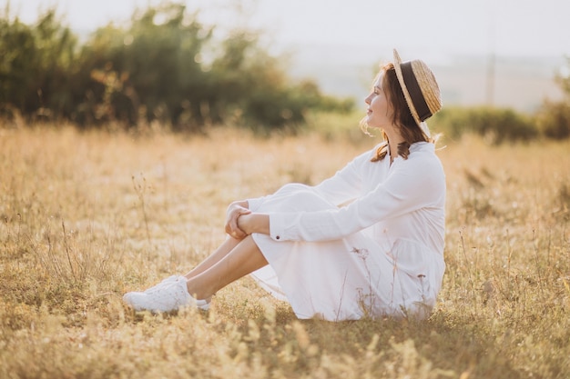 Young woman sitting in white dress and hat on the ground