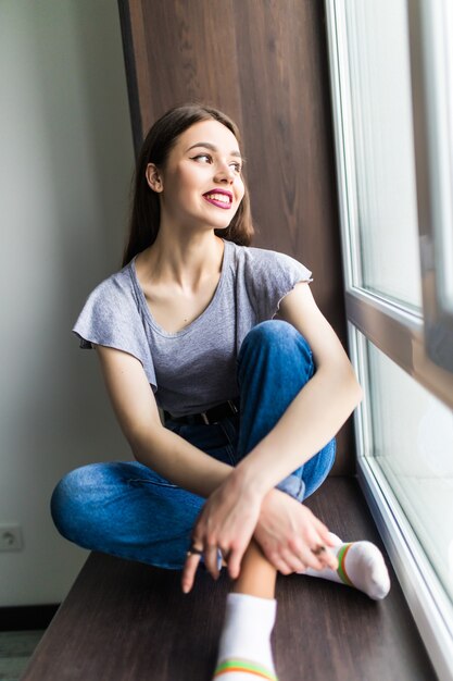 Young woman sitting on a windowsill by the window with a city view in the morning.