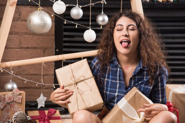 Free photo young woman sitting with boxes of christmas presents and showing tongue