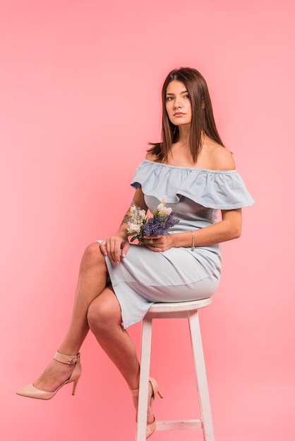 Young woman sitting with flowers bouquet on chair 