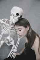 Foto gratuita giovane donna seduta con scheletro e tenendo la sua mano