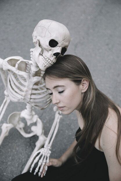 Молодая женщина, сидя с скелетом и проведение его руки
