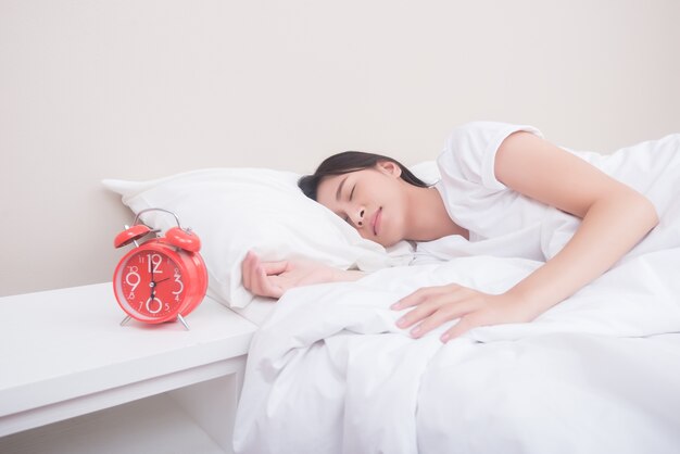 Young woman sleeping in bed beside alarm clock