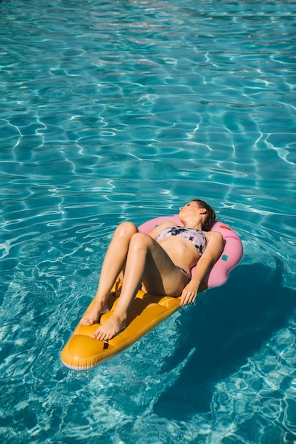 Молодая женщина спит на надувной матрас в бассейне