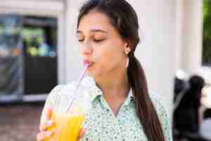 Бесплатное фото Молодая женщина улыбается и пьет коктейль со льдом в пластиковом стаканчике с соломинкой