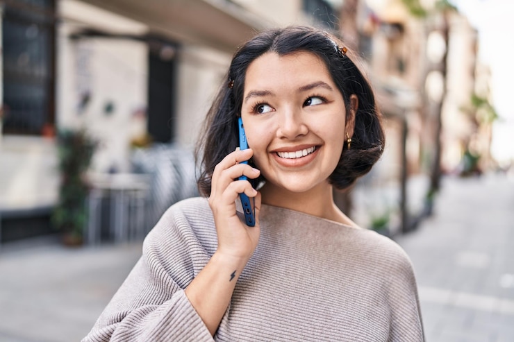 無料Photo 通りでスマートフォンで話す自信に満ちた笑顔の若い女性