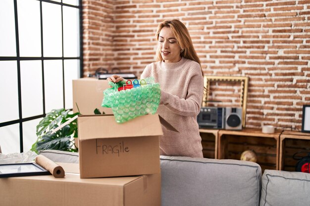 Free photo young woman smiling confident unpacking cup on cardboard box at new home