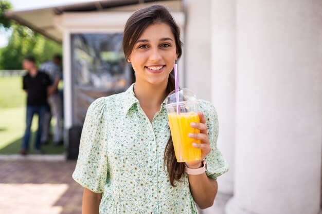 Young woman smiling and drinking cocktail with ice in plastic cup with straw