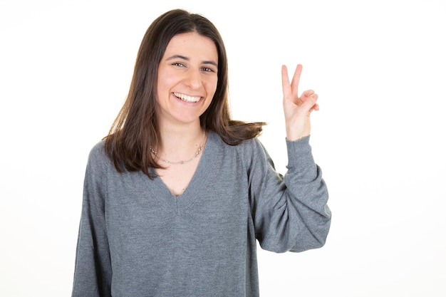 2本の指vポジティブと平和ジェスチャー白い背景を示す幸せな成功を笑顔の若い女性