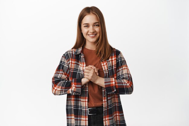 Young woman smiling holding hands clenched near chest hopeful, asking for something, hoping, begging to have chance, standing against white background