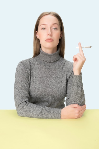 Молодая женщина курит сигарету, сидя за столом в
