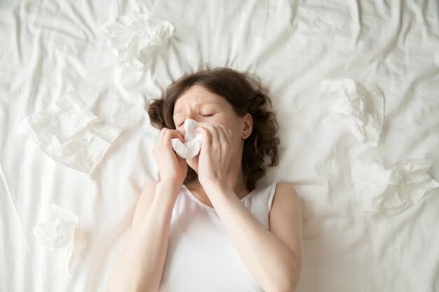 Young woman sneezing into tissue