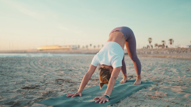 Young woman in sport clothes doing yoga exercise on the beach Pretty girl doing stretching exercises