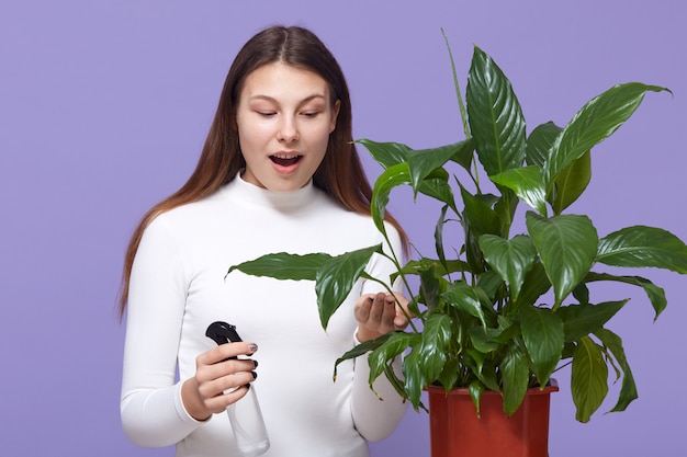 Молодая женщина опрыскивает растения в вазонах и смотрит на цветок в горшке с широко раскрытым ртом