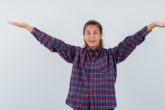 Young woman spreading arms as greeting someone in checked shirt and looking pretty