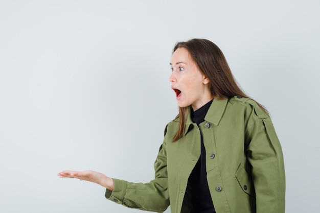 Giovane donna che allarga il palmo da parte mentre urla a qualcuno in giacca verde, camicia nera e sembra aggressivo, vista frontale.