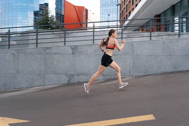 朝の屋外で全力疾走する若い女性。市内で運動している女性ランナーの側面図。