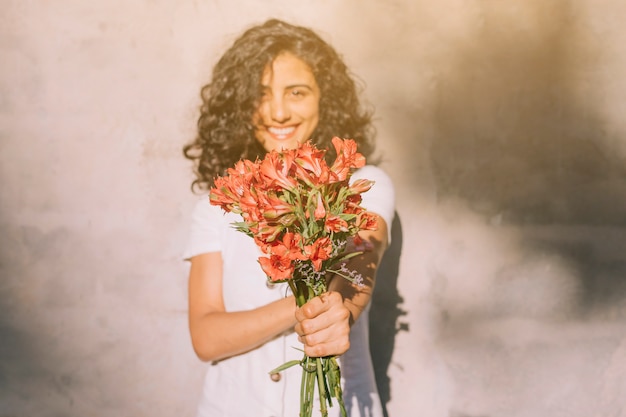 手でアルストロメリアの赤い花の花束を持って壁に立っている若い女性