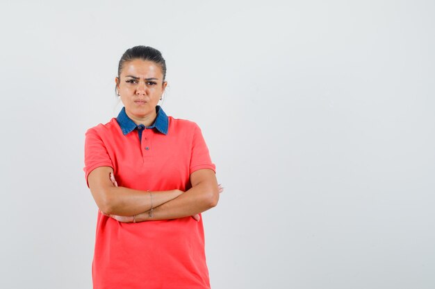 Young woman standing arms crossed in red t-shirt and looking displeased. front view.