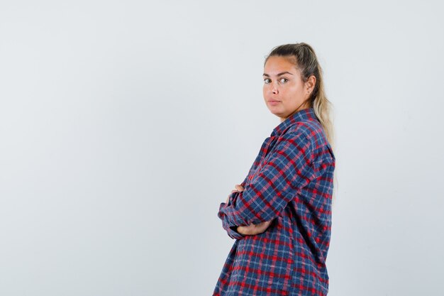 Young woman standing arms crossed while looking over shoulder in checked shirt and looking pretty