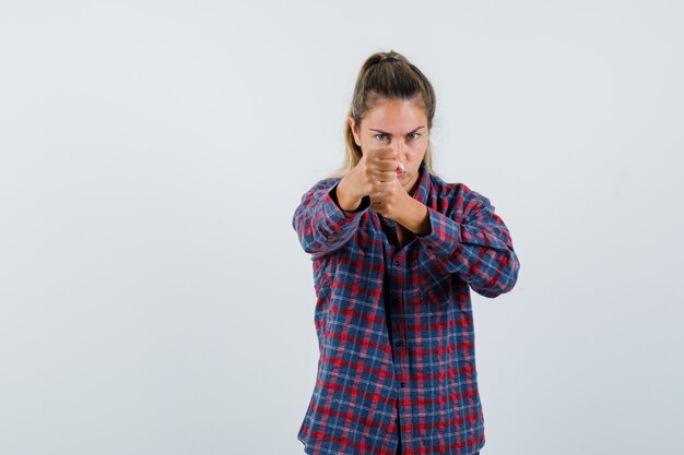 Young woman standing in boxer pose in checked shirt and looking confident