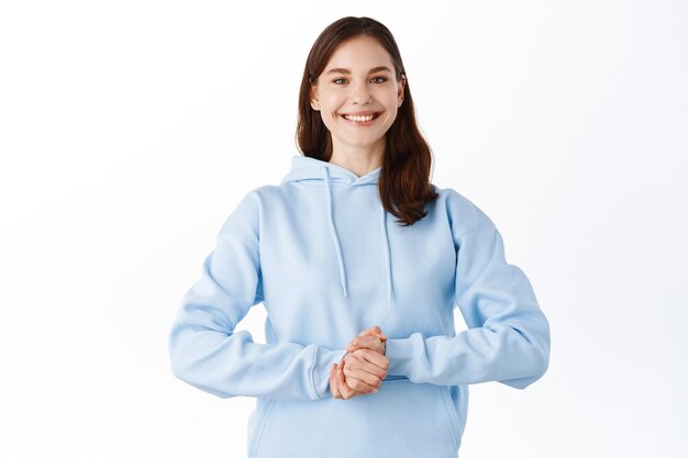 Young woman standing confident and happy, gladly answer your questions, standing over white wall