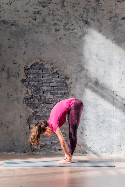 Free photo young woman standing on exercise mat doing stretching exercise