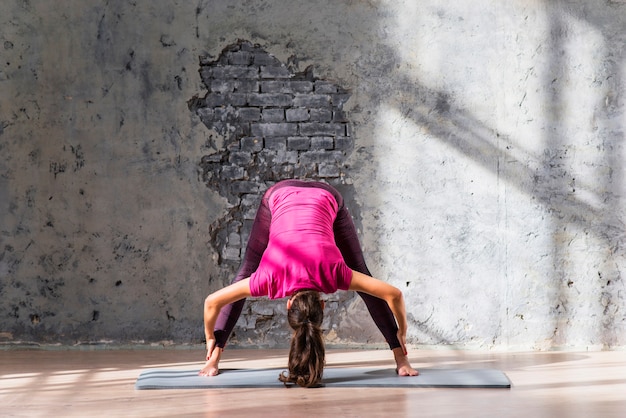 Young woman standing on exercise mat practicing yoga