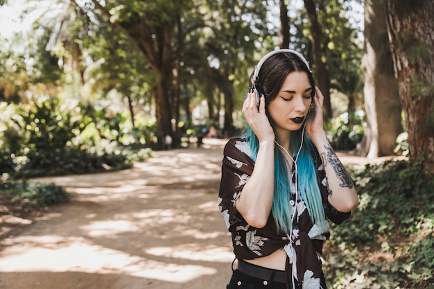 헤드폰에 숲 듣는 음악에 서있는 젊은 여자