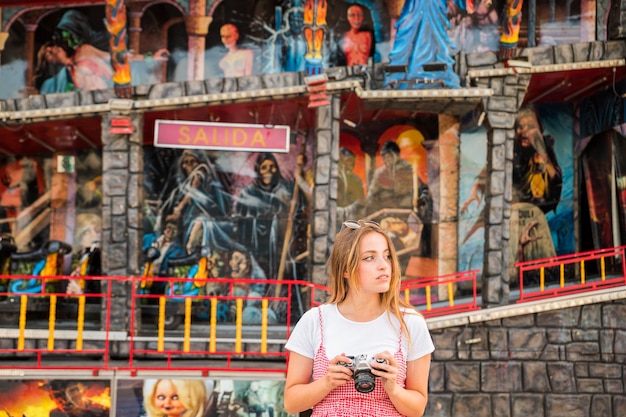 Young woman standing in front of haunted house fun ride holding camera