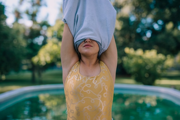 Young woman standing in front of swimming pool removing the clothes