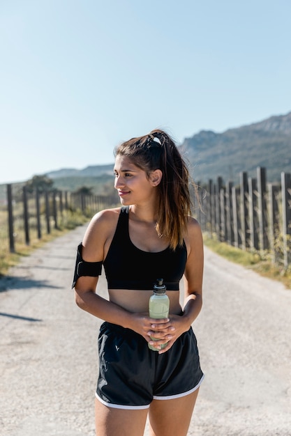 Free photo young woman standing and holding bottle with energetic drink