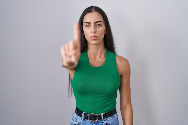 Молодая женщина, стоящая на изолированном фоне, указывая пальцем вверх и сердитым выражением лица, не показывая жеста
